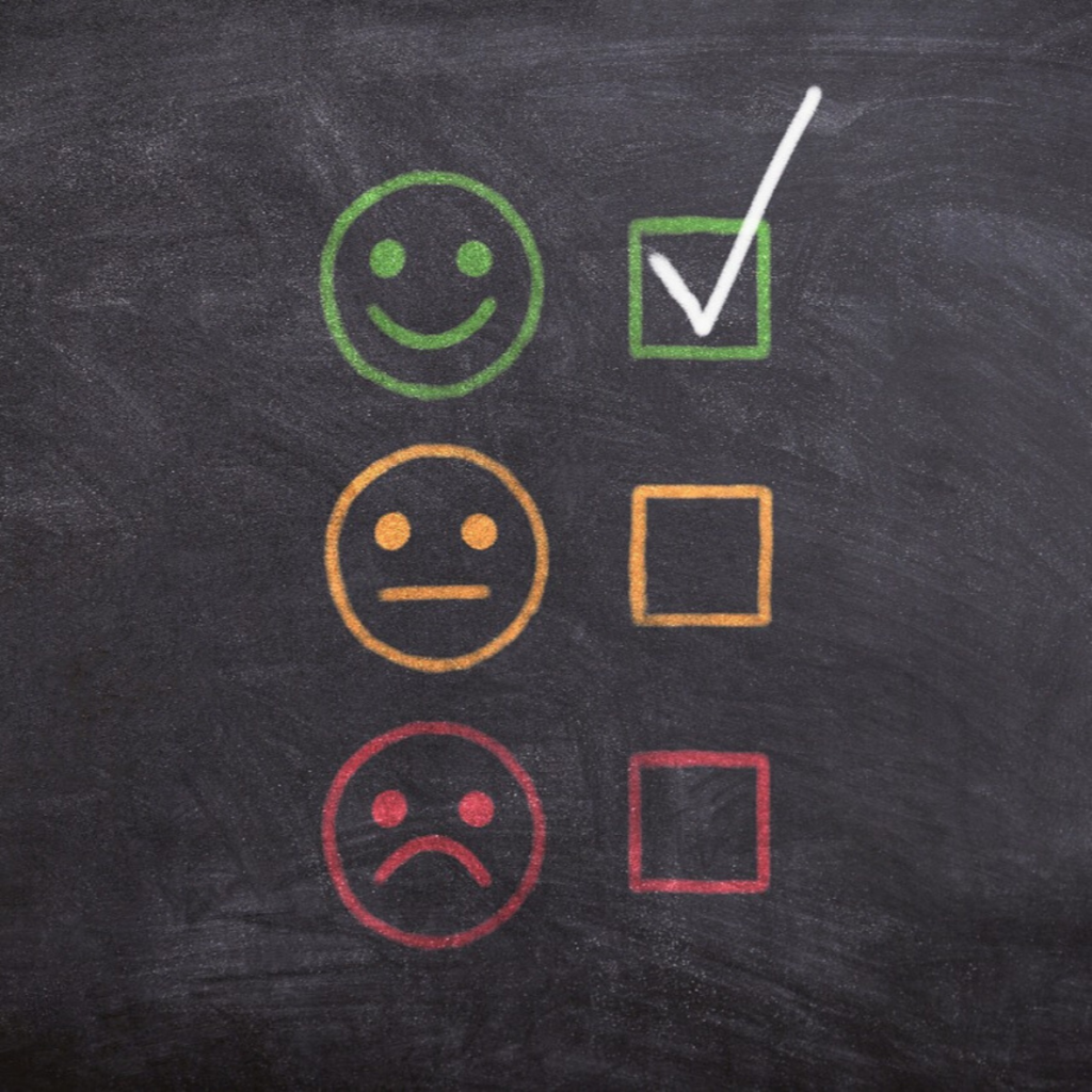 A customer satisfaction survey drawn in chalk with smiling, neutral and sad faces and a checked box on a blackboard.