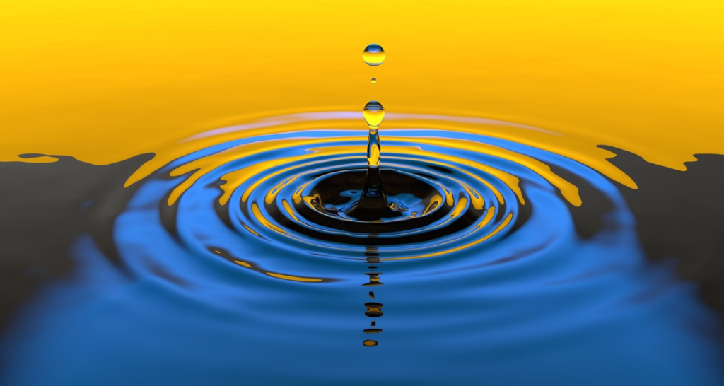 Goutte d'eau tombant sur une surface, créant des ondulations concentriques sur fond bleu et or.