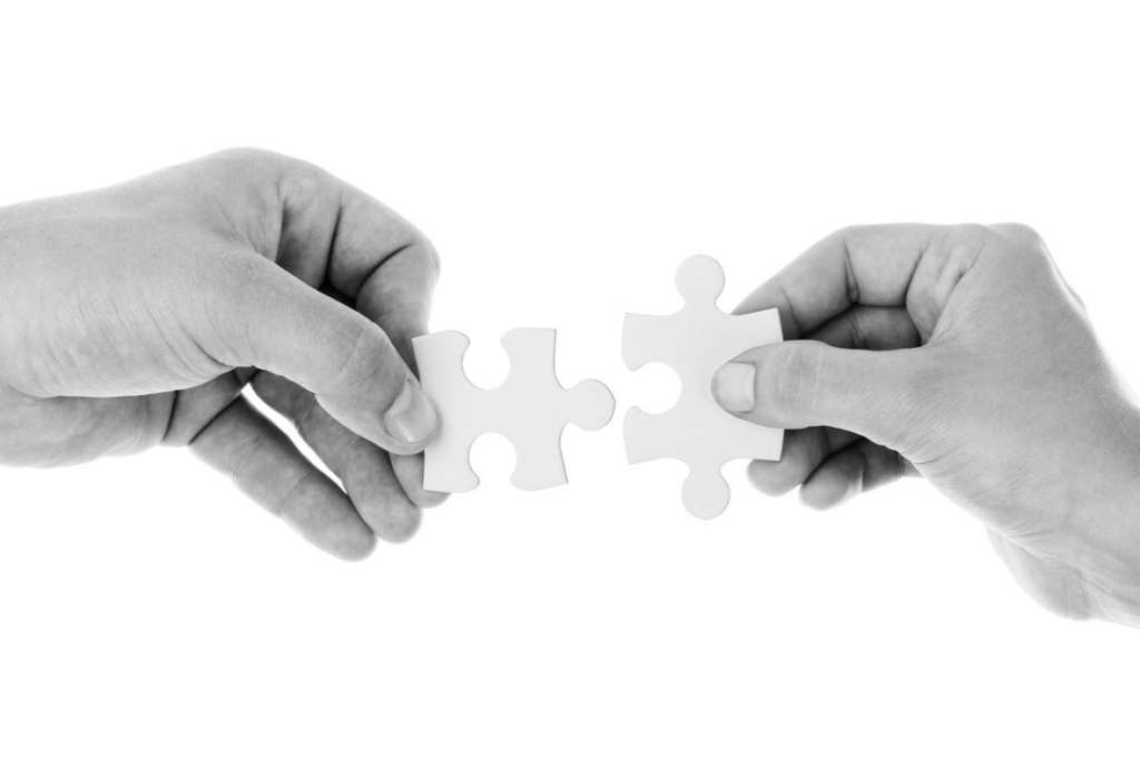 Two hands holding puzzle pieces, about to connect them, isolated on white background.