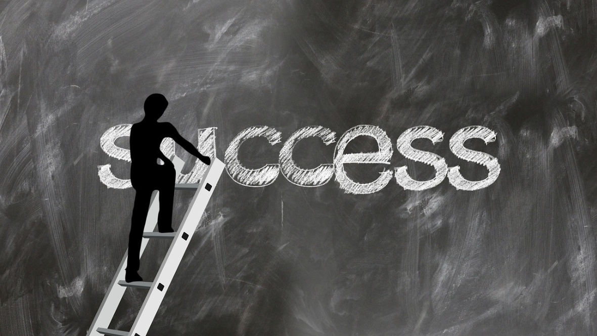 Silhouette of a person on a ladder drawing the word “success” on a chalkboard background.