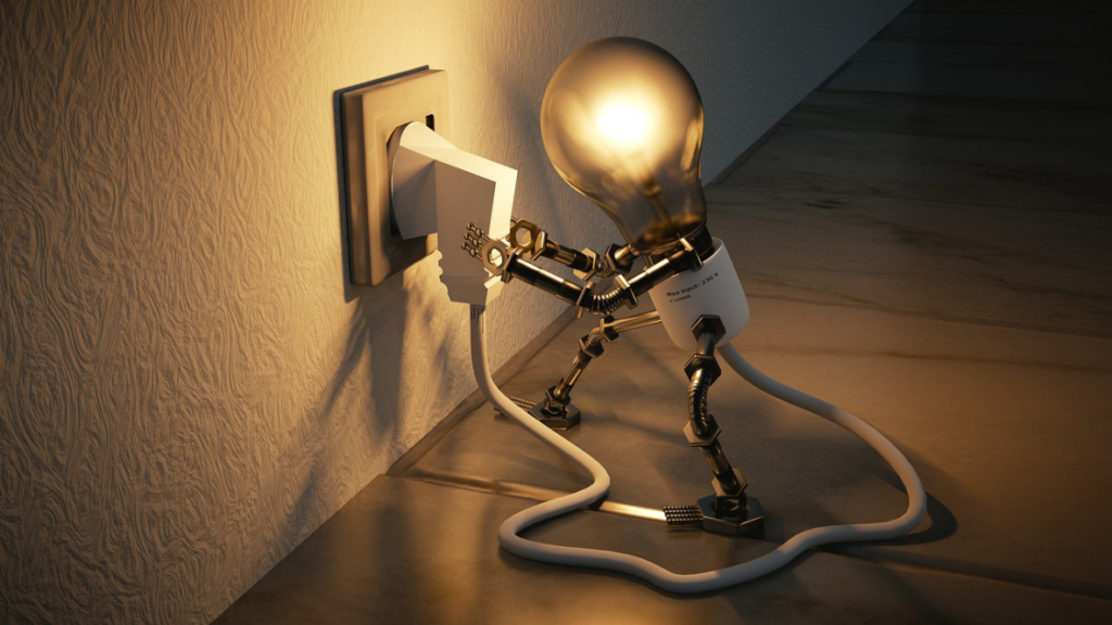 A robotic figure with a light bulb for a head plugs a cord into a wall outlet, illuminating itself in a dimly lit room.