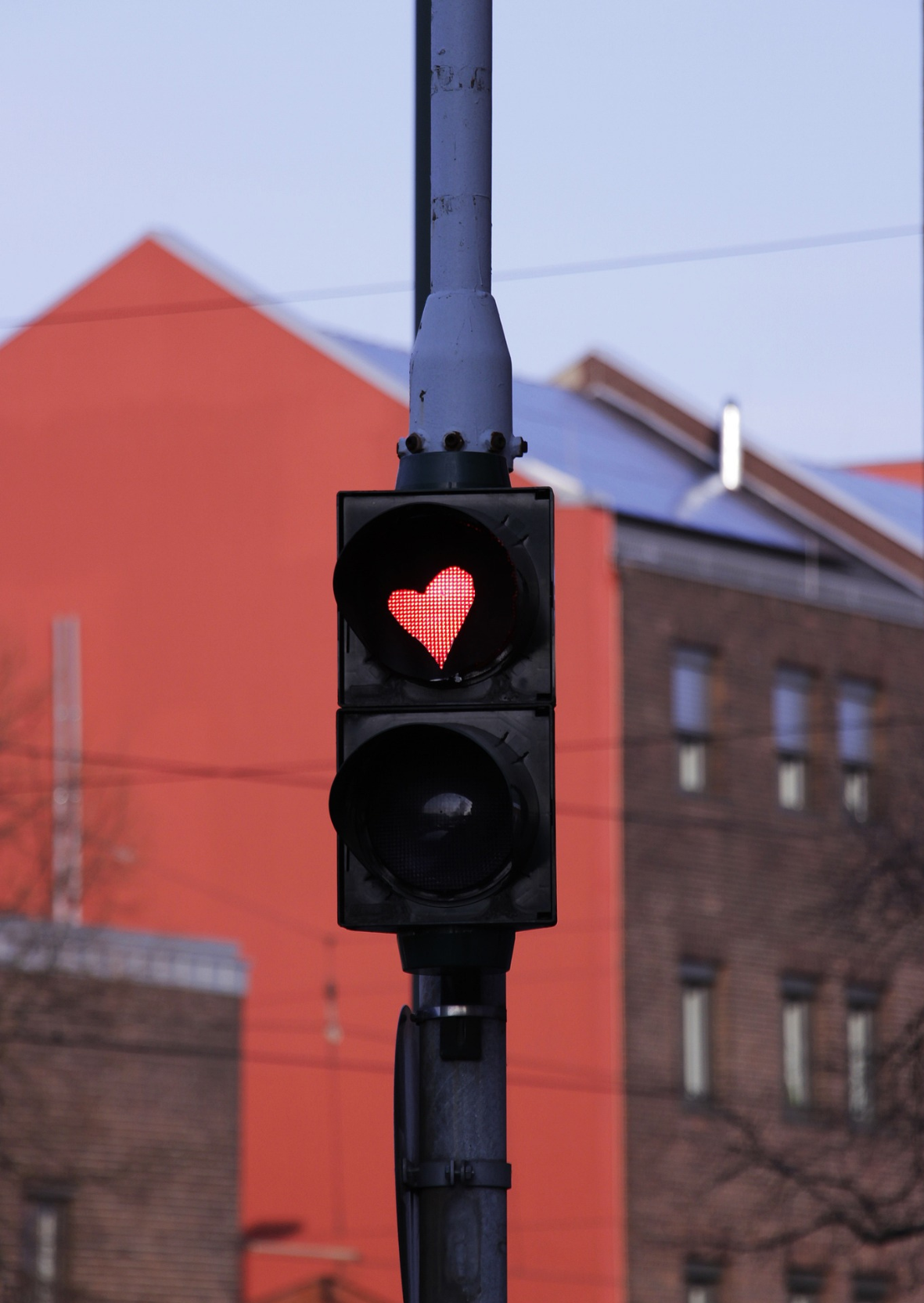 Un feu de circulation affichant un symbole de cœur rouge sur un fond urbain flou avec un bâtiment rouge.