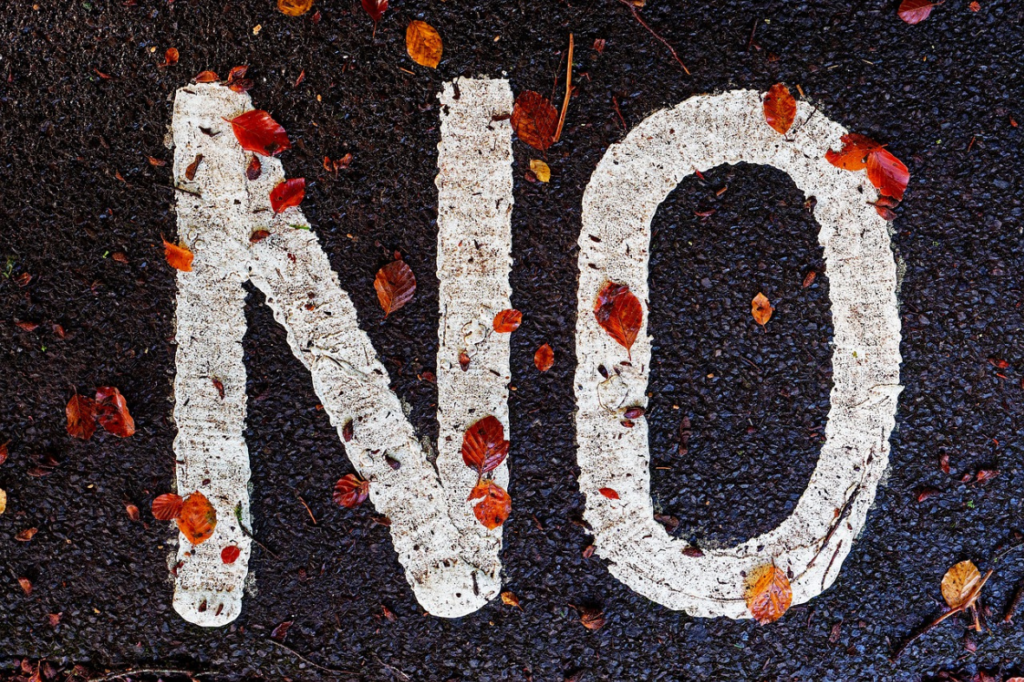 «non» peint en blanc sur une surface asphaltée sombre avec des feuilles d'automne éparses.