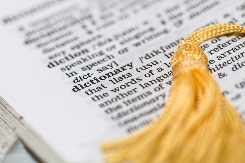 Un gros plan d'une page de dictionnaire centré sur le mot "dictionnaire", avec une houppe jaune posée sur la page - une image idéale pour tous ceux qui cherchent à comprendre les RH et à maîtriser la terminologie clé.