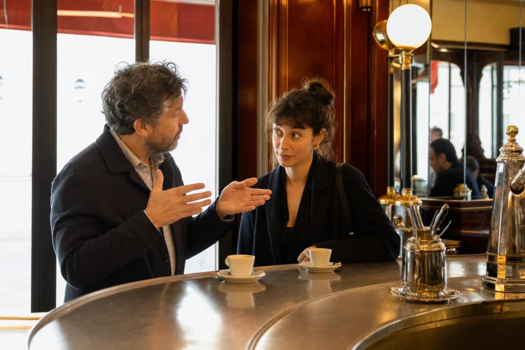 Two people at a bistro counter, one explaining with their hands, the other listening with a raised eyebrow