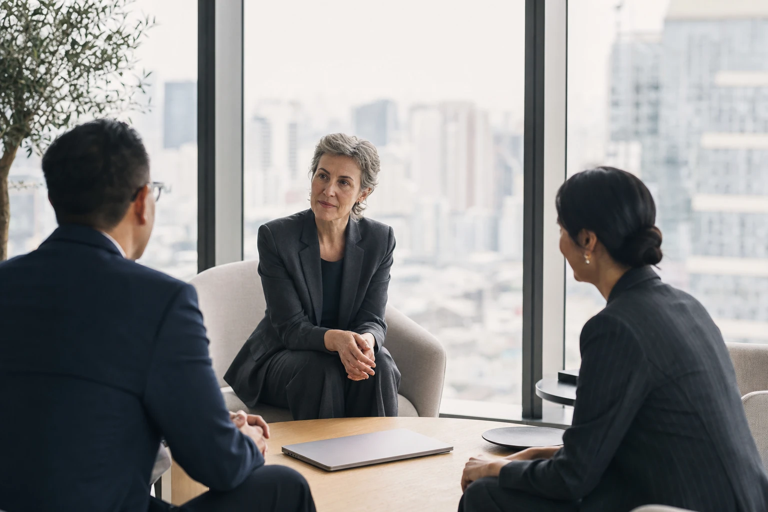 An HR consultant in discussion with two executives from a foreign head office in a bright, sober meeting room.