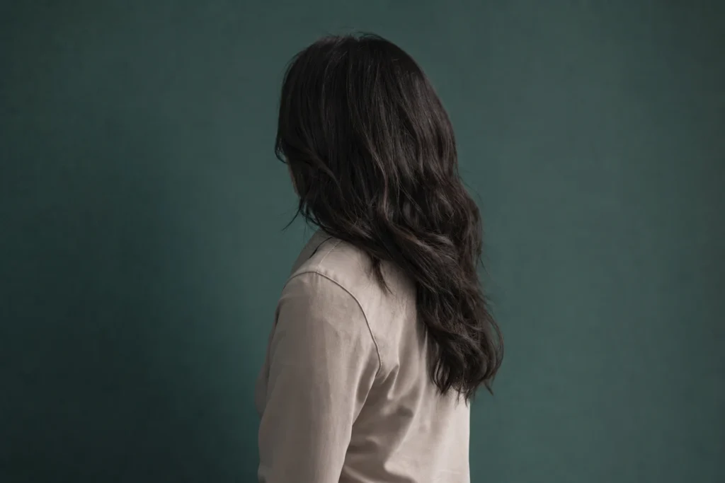 A single person standing against a plain teal wall, seen from a three-quarter rear angle
