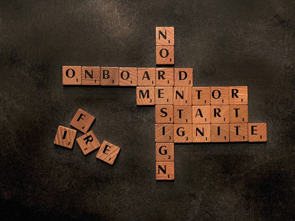 Lettres de Scrabble en bois formant les mots onboarding, mentor, start et ignite sur une surface sombre.